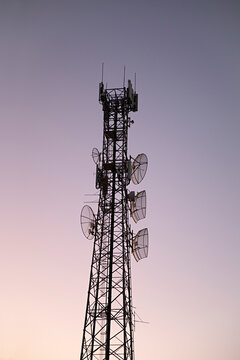 Cellular network tower with multiple antennas and dishes against a twilight sky