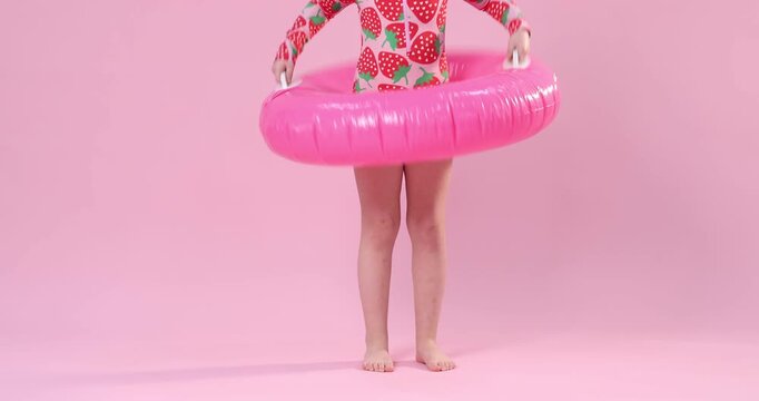 Little girl in swimsuit with inflatable ring and sunglasses on pink background