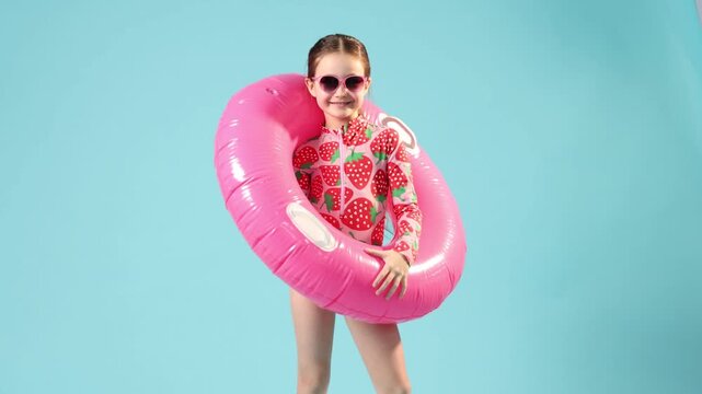 Little girl in swimsuit with inflatable ring on light blue background