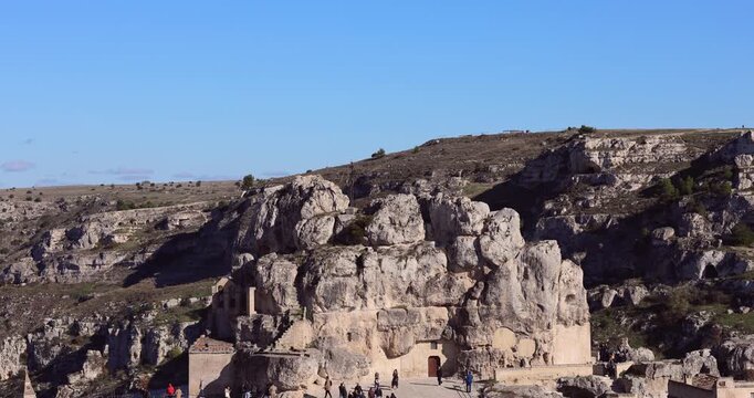 panoramic view of the ancient sassi di matera rock church and cave dwellings carved into the limestone cliffs of a rugged italian ravine under a clear blue sky.