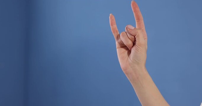 Woman showing sign of horns on blue background, closeup