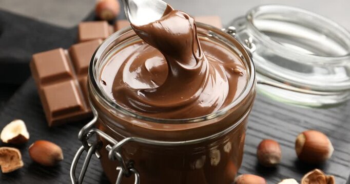 Taking tasty chocolate paste with spoon from jar at grey table, closeup