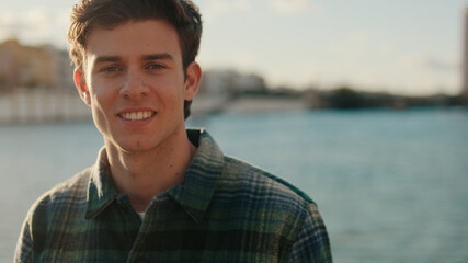 Fototapeta premium Smiling Young Man By Riverbank At Sunset