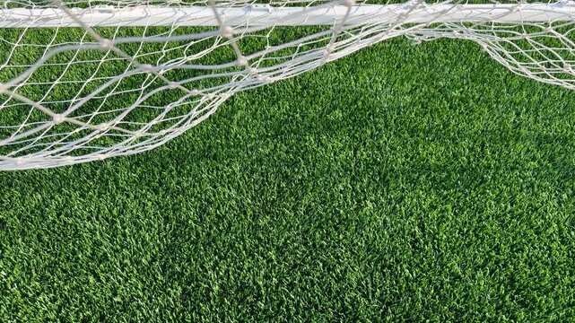 Soccer Goal Net Set Against New Turf Field. A white soccer net blows in the wind, set against newly laid green synthetic turf field. Overhead view with ample room for copy space.