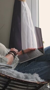 Vertical screen Woman Coding Comfortably. Casual Female Worker Multitasking With Her Laptop In Comfortable Corner. Relaxed Woman Attentively Engaged In Programming Tasks While Relaxing In Cozy Nook