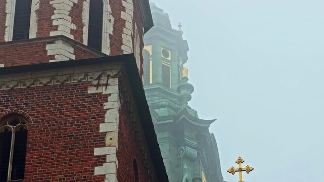Foggy morning view of a brick clocktower at Wawel Royal Castle in Krakow, Poland, with a historic church dome fading into mist and a moody Old Town skyline.