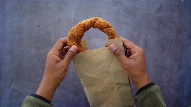 Hands holding fresh sesame simit bread over dark surface in professional cinematic footage.