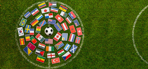Soccer ball surrounded by international flags arranged in a circle on green grass field. Concept of world cup, global football tournament, international unity and world championship with copy space. © Leonardo