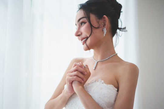 Excited Asian bride looking out window while preparing for wedding ceremony