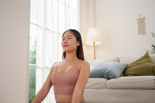 Peaceful Asian woman sitting and meditating with eyes closed at home