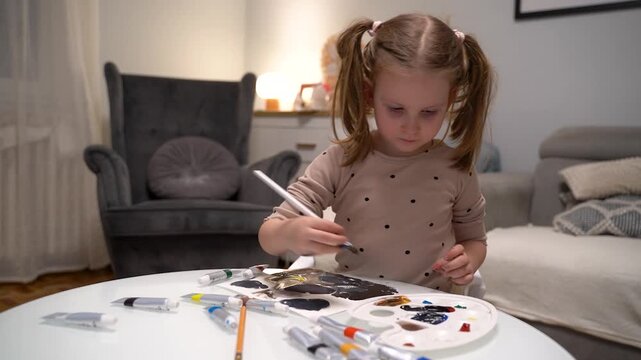Cute little girl painting at home in her room with tempera paints 