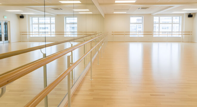Bright and spacious interior of an empty modern dance studio featuring wooden floors large mirrors and a wooden barre handrail