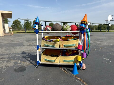 Recess Play Equipment: A mobile cart filled with colorful balls, cones, and hoops on a blacktop field, ready for healthy outdoor play and exercise.