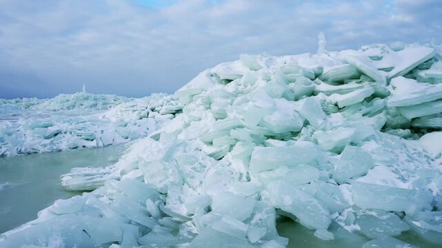 Close view of a massive sea-ice pressure ridge with blue ice slabs and slushy meltwater under a cloudy sky. Dramatic arctic texture showing fragile winter conditions.
