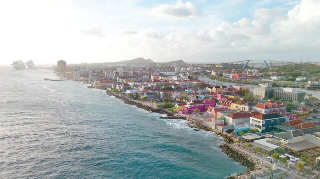 Slow aerial along Pietermaai during sunset revealing colorful UNESCO style buildings, oceanfront homes and a cruise ship.