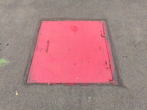 Bright Red Metal Manhole Cover Set in Asphalt Pavement.