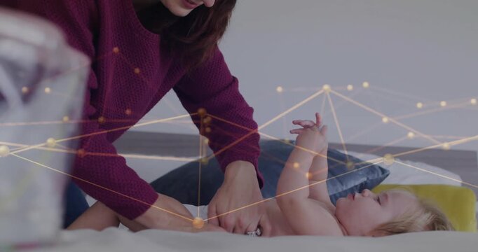 Mom sliding tabs and changing diaper for health while baby holding teether, nodes floating over bed