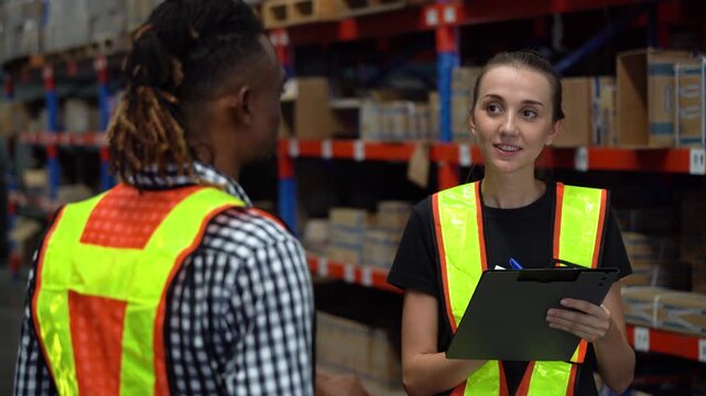 Diverse warehouse workers during training. African supervisor pointing and mentoring Caucasian woman with clipboard. Teamwork, communication, and staff development in logistics distribution center.