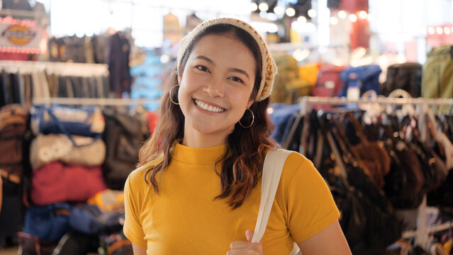 Young teen Gen Z asia female happy smile looking at camera at zero waste eco go green buy second hand sale store flea market mall thrift old used vintage fabric retro style. Woman people enjoy shop.