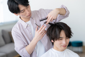Naklejka premium ヘアサロンでヘアカットをしてもらう若い男性