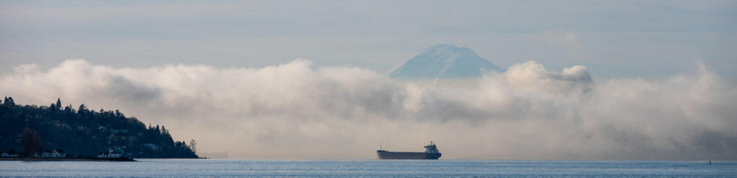 Bulk carrier cargo ship in Puget Sound on a foggy morning with air full of exhaust and pollution, Mt. Rainier in background, global shipping of trade goods worldwide, import and export 