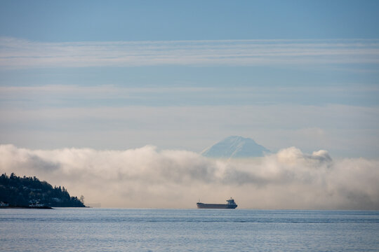 Bulk carrier cargo ship in Puget Sound on a foggy morning with air full of exhaust and pollution, Mt. Rainier in background, global shipping of trade goods worldwide, import and export 