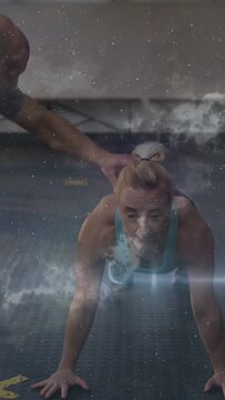 Vertical video: Woman doing push-ups in gym, coach cueing form, faint star overlay softly obscuring