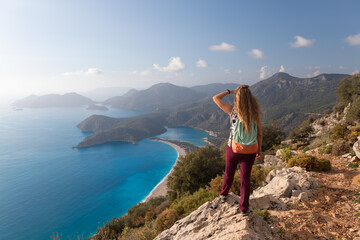 Fototapeta premium Young woman looking at Oludeniz beach, blue lagoon with clear bright turquoise water, Lycia coast. Summer day walk by Lycian way at family vacation in Mediterranean Sea, Fethye, Antalya region, Turkey