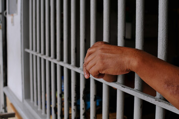 Obraz premium Close up of a prisoner hand gripping rusty iron bars behind a jail cell or detention center.