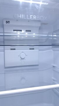 Panning Shot of Clear interior shows modern chiller box with control panel. White surfaces reflect soft lighting for clean, minimalist look. Empty shelves suggest spacious storage for drinks or food