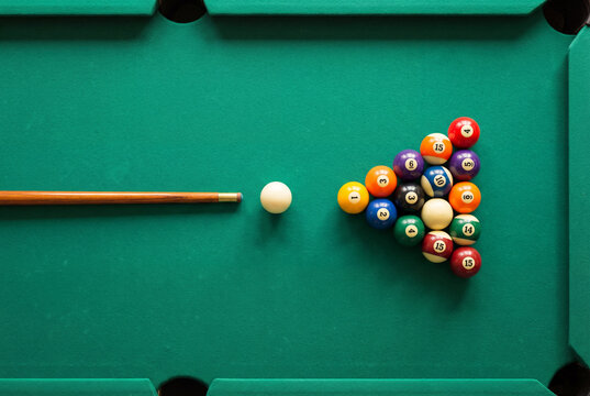 Billiard balls racked in a triangle on a green pool table with a cue stick and ball