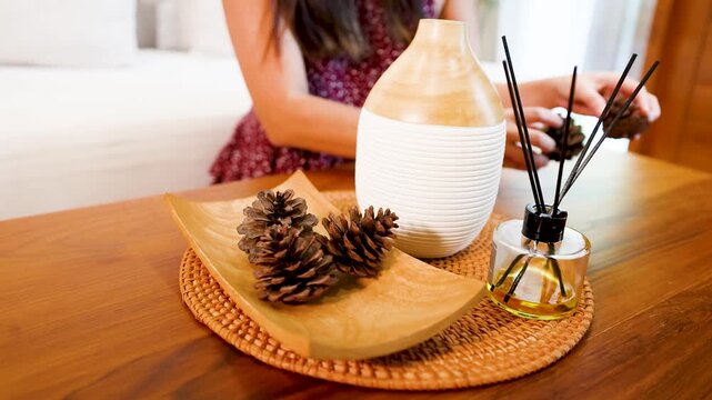 Asian Woman Arranging Pine Cones Near Essential Oil Diffuser on Table