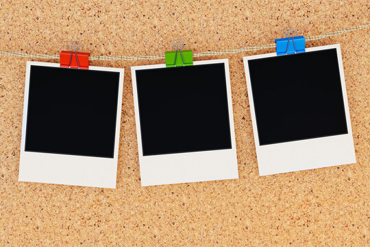 Three Blank Instant Photo Frames Hanging on Rope with Colorful Binder Clips on Cork Board Background &mdash; Copy Space Mockup