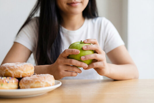 Woman choosing a healthy green apple over a plate of sweet donuts