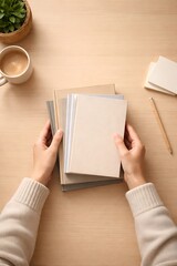Fototapeta premium Overhead view of hands holding a stack of notebooks on a wooden desk with a coffee cup and plant.