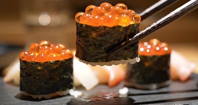Close-up of sushi with vibrant salmon roe being picked up with chopsticks in a cozy restaurant