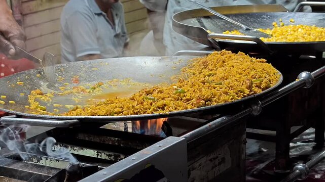 Street vendor stirring spicy tawa pulav fried rice with vegetables on a large flat pan