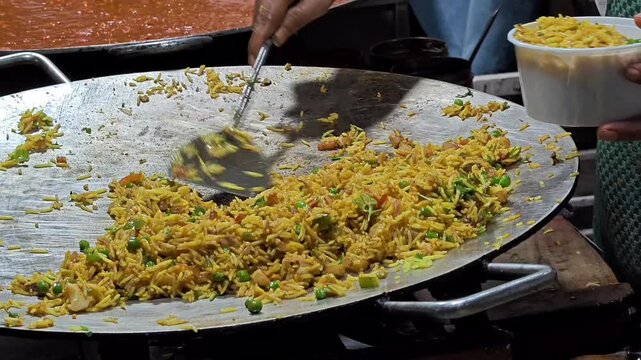 Street vendor stirring spicy tawa pulav fried rice with vegetables on a large flat pan