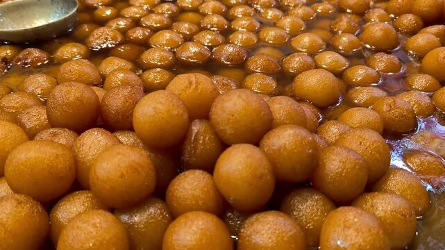 Close up of traditional indian sweet gulab jamun being dipped in warm sugar syrup