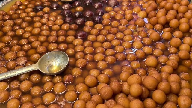 Close up of traditional indian sweet gulab jamun being dipped in warm sugar syrup