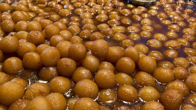 Close up of traditional indian sweet gulab jamun being dipped in warm sugar syrup