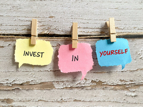 Invest in yourself message on colorful paper notes clipped on a string with wooden background, motivation and self growth concept.