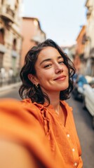 Fototapeta premium Young Woman Posing in Vibrant Orange Blouse for Selfie on Street
