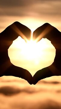 A silhouette of hands forming a heart shape against a bright golden sunset above the clouds