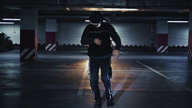 Energetic man wearing headphones dancing freely in a dim, empty underground parking garage