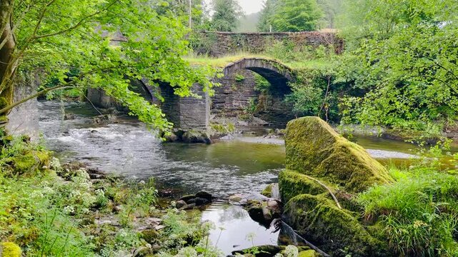 Watersmeet Bridge with old stone arches over flowing river surrounded by green trees rocks and natural woodland creating scenic calm outdoor landscape