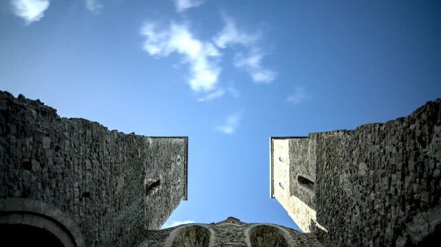 Upward view of Corfe Castle with medieval stone towers rising against bright blue sky and clouds showing historic architecture and dramatic perspective