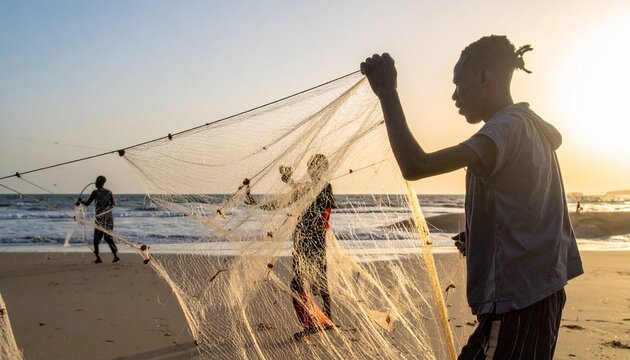 夕暮れの砂浜で力を合わせて漁網を引くアフリカの漁師たち