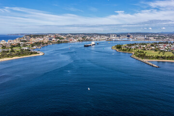 Fototapeta premium Aerial drone view of a large cargo ship being escorted by tug boats through Newcastle Harbour in New South Wales, Australia.