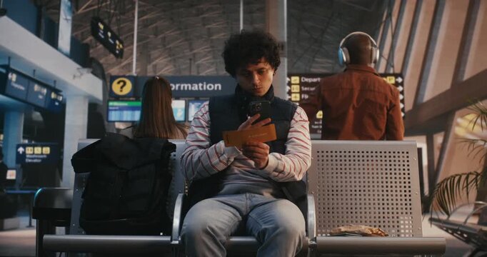 Young Man in Striped Shirt Finishes Snack, Takes out Smartphone, Scans Digital Boarding Pass. Male Grabs Black Backpack From Seat and Confidently Walks Through Airport Terminal Toward Departure Gate.
